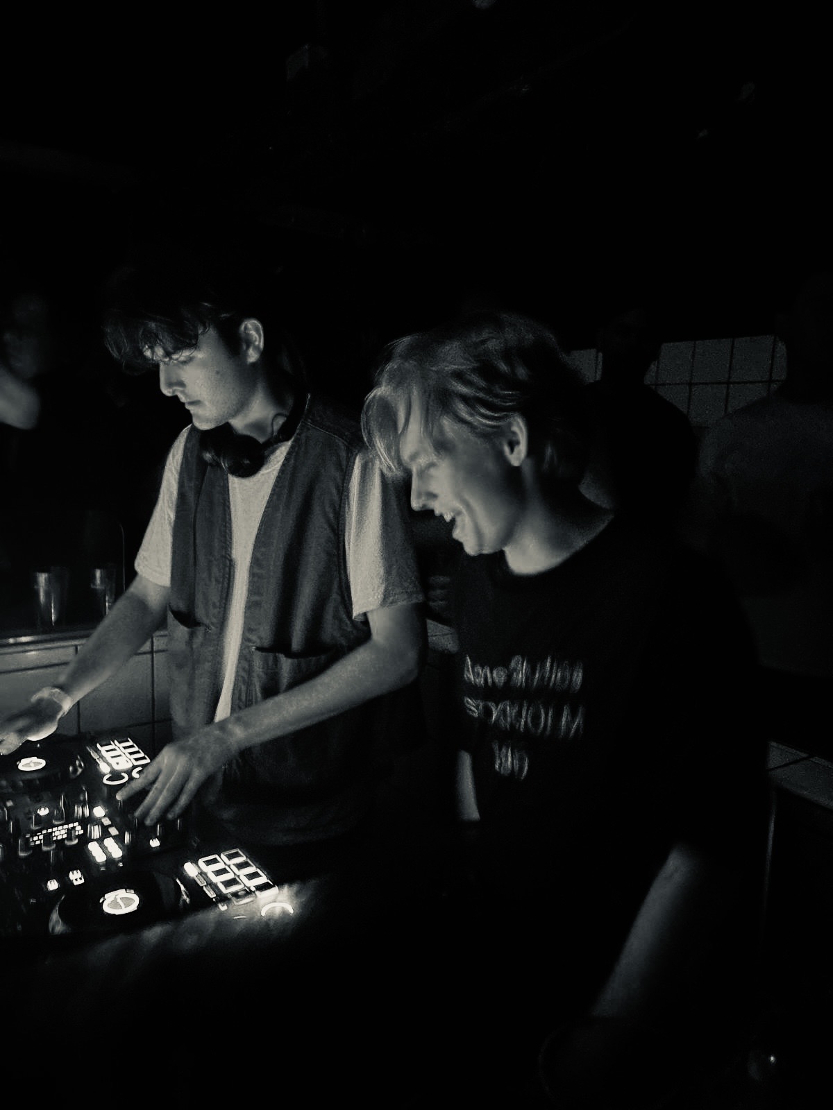 A candid black-and-white photo of two DJs performing together behind the decks